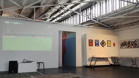 Image of world cup football game projected on wall of Lil Homey Cafe with artwork adjacent wall