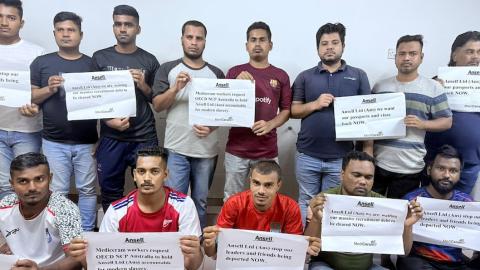 Bangladeshi migrant workers hold signs demanding Ansell take responsibility for addressing MediCeram labour violations.