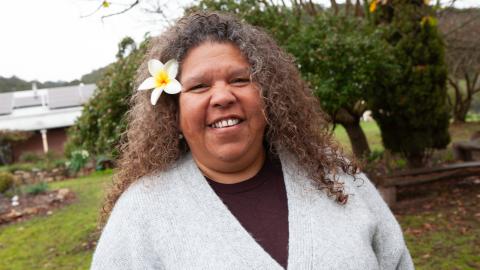 Image of Karina Lester, a Yankunytjatjara Anangu leader, second-generation survivor of British nuclear tests at Emu Field in South Australia, ICAN Ambassador, and Commissioner on the AUKUS Public Inquiry. She has a frangipani in her hair.