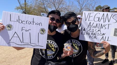 Photo of Claire and Jesse smiling and holding up signs saying Liberation for All and Vegans Against Fascism